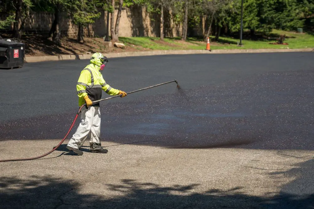 A man in yellow jacket spraying water on asphalt.